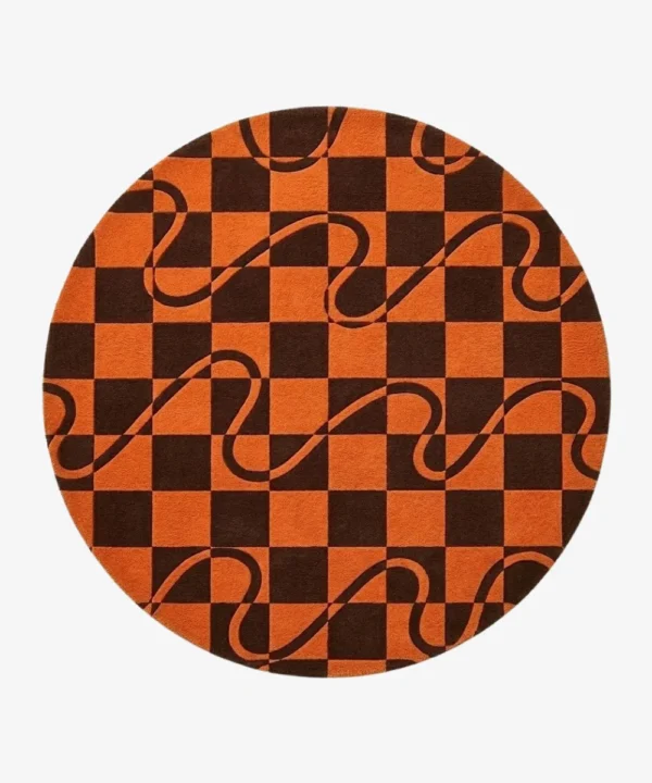 A top-down studio product photograph of a round area rug featuring a geometric orange and dark brown checkerboard pattern overlaid with flowing wavy lines.