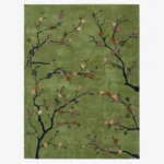 A top-down studio product photograph of a rectangular area rug with a sage green background featuring delicate black cherry blossom branches and colorful floral accents.
