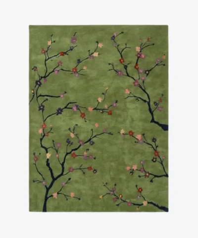 A top-down studio product photograph of a rectangular area rug with a sage green background featuring delicate black cherry blossom branches and colorful floral accents.