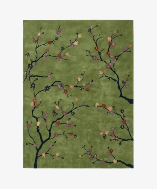 A top-down studio product photograph of a rectangular area rug with a sage green background featuring delicate black cherry blossom branches and colorful floral accents.