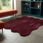 An angled perspective shot of the deep red scalloped rug, highlighting its unique wavy edge and its placement in a contemporary home setting.