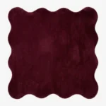 A top-down studio product photograph of a solid deep red, scalloped-edge area rug featuring a plush, textured pile on a clean white background.