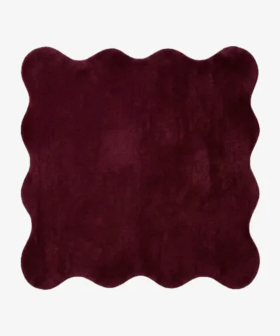 A top-down studio product photograph of a solid deep red, scalloped-edge area rug featuring a plush, textured pile on a clean white background.