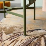 A close-up perspective of the leg of a green chair resting on the Savannah Pride area rug, highlighting the intricate texture of the leopard-themed wildlife artwork.