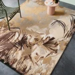 A high-angle interior shot of the rectangular Savannah Pride area rug featuring a detailed leopard wildlife motif in earthy tones, styled with a green chair, small table, and decorative bowl.