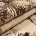 A macro view of the folded Savannah Pride area rug, showcasing the plush, dense pile and the detailed craftsmanship of the leopard and grassy landscape design.