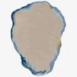 A top-down studio product photograph of a unique, irregularly shaped abstract area rug featuring a neutral beige center surrounded by layered ocean-inspired blue, turquoise, and gold wavy borders.