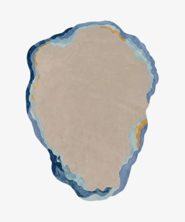 A top-down studio product photograph of a unique, irregularly shaped abstract area rug featuring a neutral beige center surrounded by layered ocean-inspired blue, turquoise, and gold wavy borders.