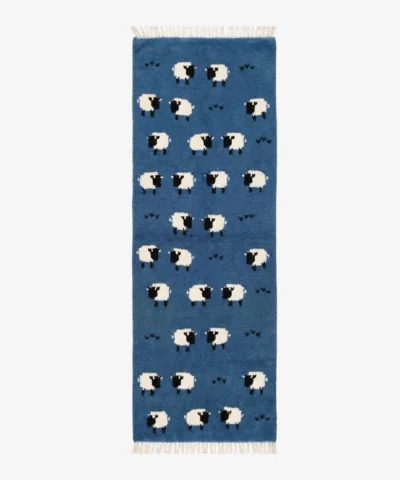Top-down product shot of a rectangular blue wool runner rug featuring a playful, repeating pattern of white and black sheep and small dark heart motifs.