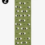Top-down studio photograph of a rectangular green wool runner rug featuring a repeating pattern of stylized white and black sheep.