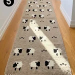 Perspective shot of a taupe-colored Sleep Sheep wool runner rug featuring a repeating sheep pattern, styled in a sunlit residential hallway.