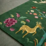 Angle view of the handmade Verdanis tufted rug showcasing its detailed botanical and wildlife illustrations on a green field.