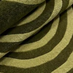 Close-up of the plush tufted pile texture, deep olive and sage green color blocking, and soft rolled edge on the Virel Torelix rug.