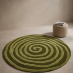 Virel Torelix round green spiral pattern tufted area rug styled in a modern interior setting with a textured pouf.