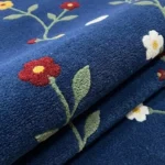 A close-up detail shot of the folded Wildora floral runner rug, showcasing the plush tufted wool pile, rich navy blue base, and detailed wildflower graphics.