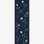 A top-down studio product photograph of a navy blue floral runner area rug featuring embroidered wildflower motifs in yellow, white, and red.