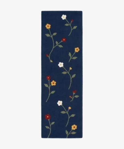 A top-down studio product photograph of a navy blue floral runner area rug featuring embroidered wildflower motifs in yellow, white, and red.