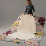 Bloomara handmade tufted area rug featuring a creamy beige center surrounded by a vibrant floral border of pink, yellow, and purple flowers, held up for display.