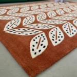 Angle view of the handmade Folivora Leaf tufted rug showcasing its rich terracotta background and detailed leaf motifs on the floor.