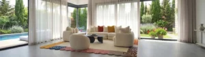 Modern living room interior featuring an organic irregular-shaped colorful bordered area rug anchored beneath a modular sectional sofa and armchairs on a large grey tiled floor.