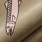 Close-up macro texture shot of the high-density tufted wool pile, carved contours, and detailed pink fish illustration on the Blush Salmon designer rug.