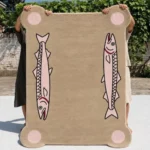 Blush Salmon tufted area rug held up vertically outdoors, showcasing its full rectangular shape, corner dot details, and pink fish motifs.
