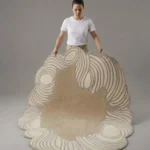 Tidewave handmade tufted area rug featuring organic beige and cream swirling wave patterns, held up for display in a studio.