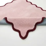 Cheeky Bloom rug with a folded corner, showing the soft pink tufted wool top, contrasting deep red scalloped edge, and durable backing underneath.