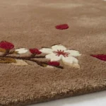 Low-angle corner view of the brown Cherrywood Bloom wool rug, highlighting the carved floral branches, white flowers, and plush texture.
