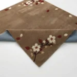 Cherrywood Bloom rug with a folded corner, displaying the detailed tufted floral pattern on top and the durable blue textile backing underneath.