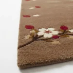 Close-up of the Cherrywood Bloom rug edge, showcasing the rich brown tufted wool pile alongside detailed white cherry blossoms and red petals.