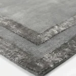 Close-up texture shot of the Gray Edge rug, showcasing the dense tufted grey wool and the detailed hand-carved finish of the metallic silver double borders.