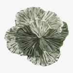 A fashion model walking past the large irregular Leaf Loop hand-tufted wool rug displayed vertically on a dark wall, highlighting its organic botanical shape and intricate green-and-white radial texture.
