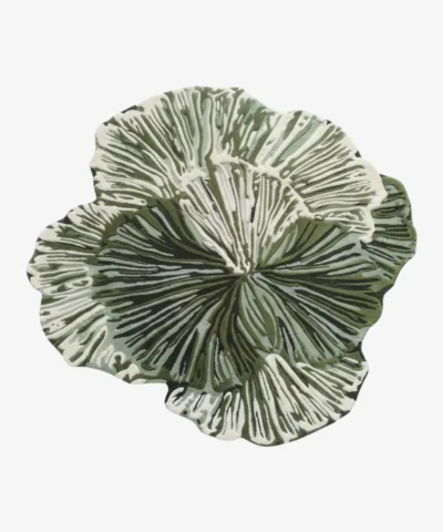 A fashion model walking past the large irregular Leaf Loop hand-tufted wool rug displayed vertically on a dark wall, highlighting its organic botanical shape and intricate green-and-white radial texture.