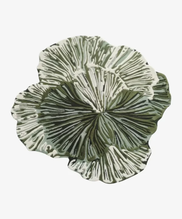 A fashion model walking past the large irregular Leaf Loop hand-tufted wool rug displayed vertically on a dark wall, highlighting its organic botanical shape and intricate green-and-white radial texture.