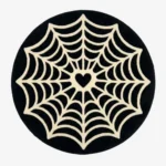 Studio flat-lay product photograph of the round Love at First Fright rug on a clean background, showcasing the black circular wool field patterned with an intricate white spiderweb design centering on a heart shape.