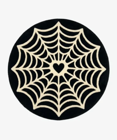 Studio flat-lay product photograph of the round Love at First Fright rug on a clean background, showcasing the black circular wool field patterned with an intricate white spiderweb design centering on a heart shape.