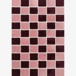 Angled studio product view of the rectangular Maroon Matrix rug, highlighting its modern checkered pattern featuring deep maroon and soft pink squares separated by clean white grout lines.