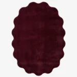 Studio flat-lay product photograph of the irregular cloud-shaped Ruby Cloud rug on a clean background, showcasing its solid deep burgundy-red wool field and unique scalloped contour border.