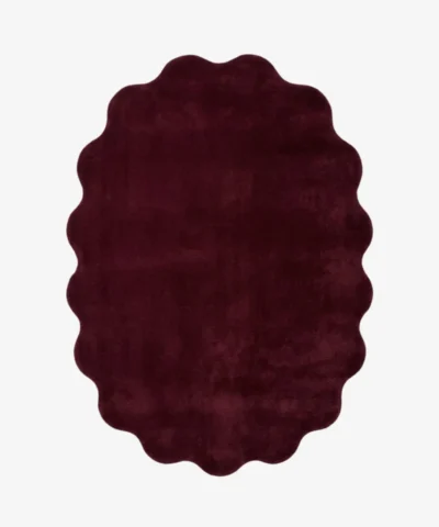Studio flat-lay product photograph of the irregular cloud-shaped Ruby Cloud rug on a clean background, showcasing its solid deep burgundy-red wool field and unique scalloped contour border.