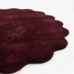 Close-up texture shot of the Ruby Cloud rug, showcasing the dense tufted deep red wool pile and the clean-cut scalloped edges.