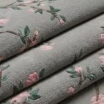 Close-up texture shot of the folded Sakura Branch rug, displaying the dense tufted grey wool and the 3D hand-carved details of the pink cherry blossoms and green foliage.