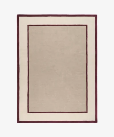 Studio flat-lay product photograph of the rectangular The Frame rug on a clean background, showcasing the neutral beige wool field framed by bold maroon-red inner and outer border lines.