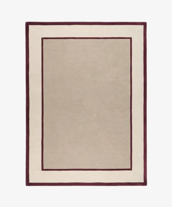 Studio flat-lay product photograph of the rectangular The Frame rug on a clean background, showcasing the neutral beige wool field framed by bold maroon-red inner and outer border lines.