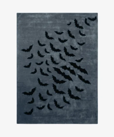 Studio flat-lay product photograph of the rectangular Wicked Batwings rug on a clean background, showcasing the grey-blue wool field patterned with a flock of black flying bats.